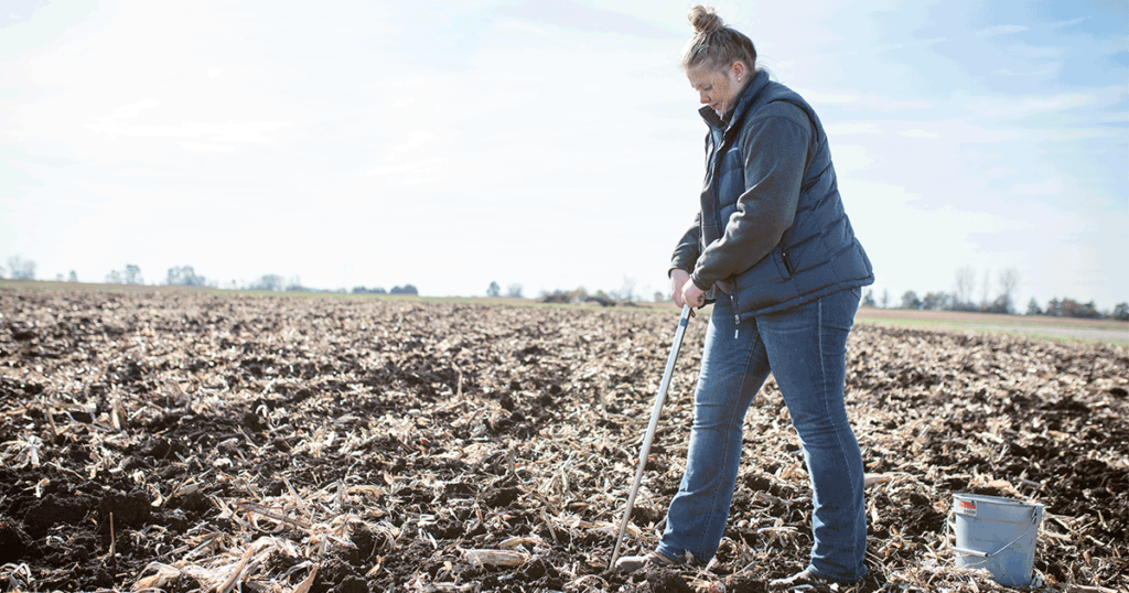 A woman samples soil in a field.